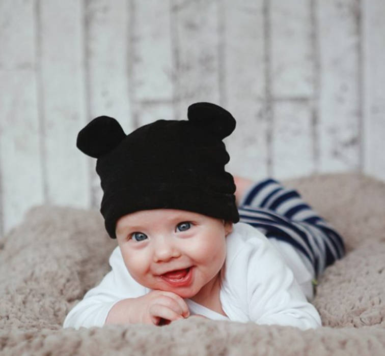 A smiling baby wearing a black mouse-ear hat, illustrating a reference in the children’s fashion industry.