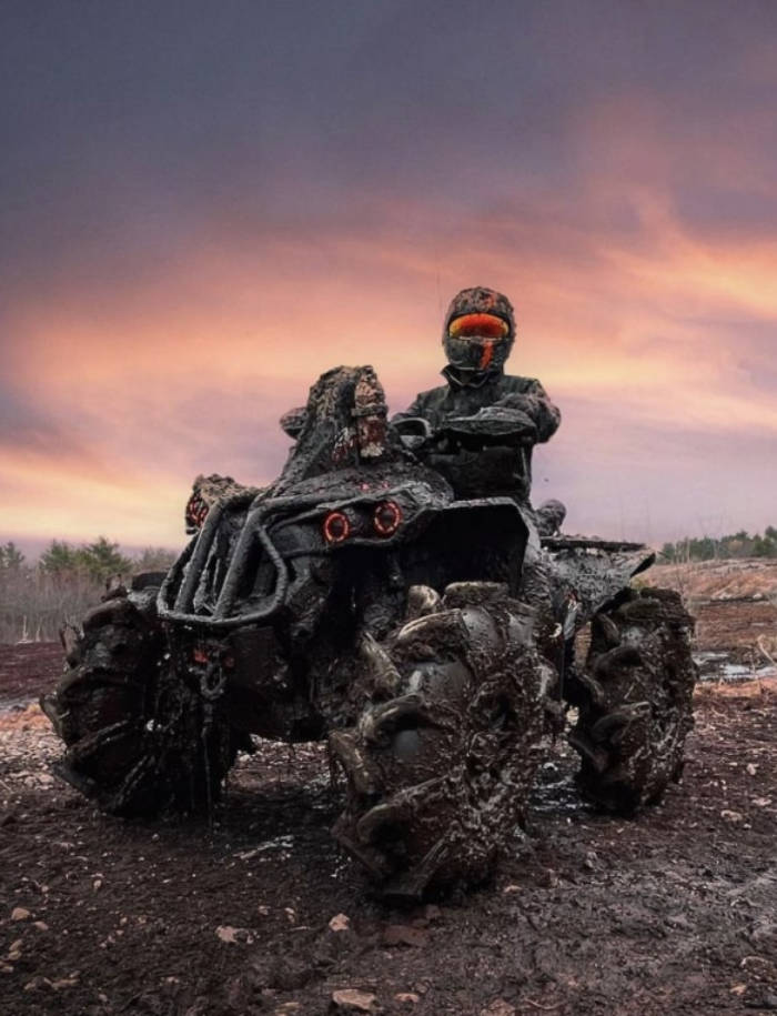 Un pilote sur un véhicule tout-terrain couvert de boue, lors d’une aventure hors-piste au coucher du soleil, représentant une entreprise de référence dans les véhicules récréatifs.