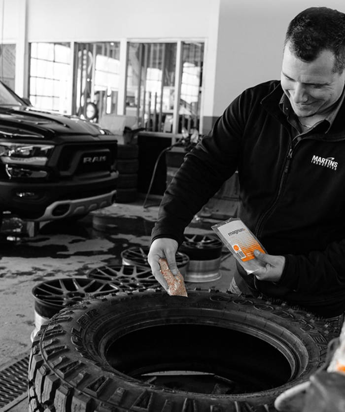 A technician using tire balancing beads in a Martins Industries workshop, with a utility vehicle in the background.