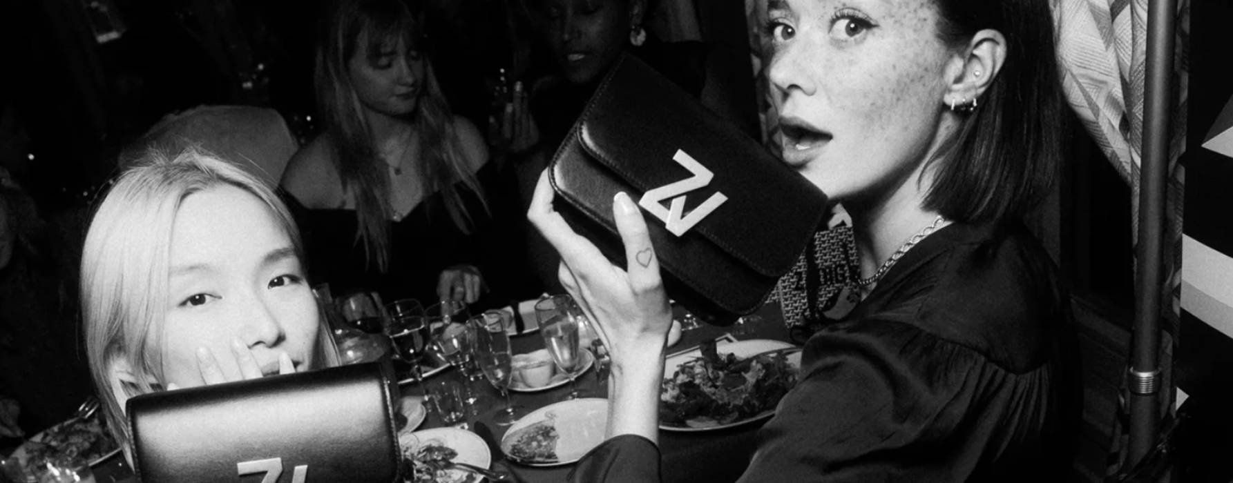 Deux femmes tenant des sacs Zadig & Voltaire lors d’une soirée élégante, entourées de convives à table.