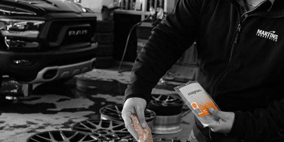 A technician applies balancing beads to a tire in a workshop with a pickup truck in the background.