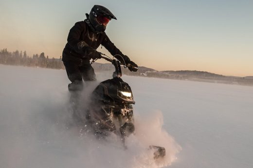 Rider on a Widescape snowmobile crossing a snowy landscape at sunset.
